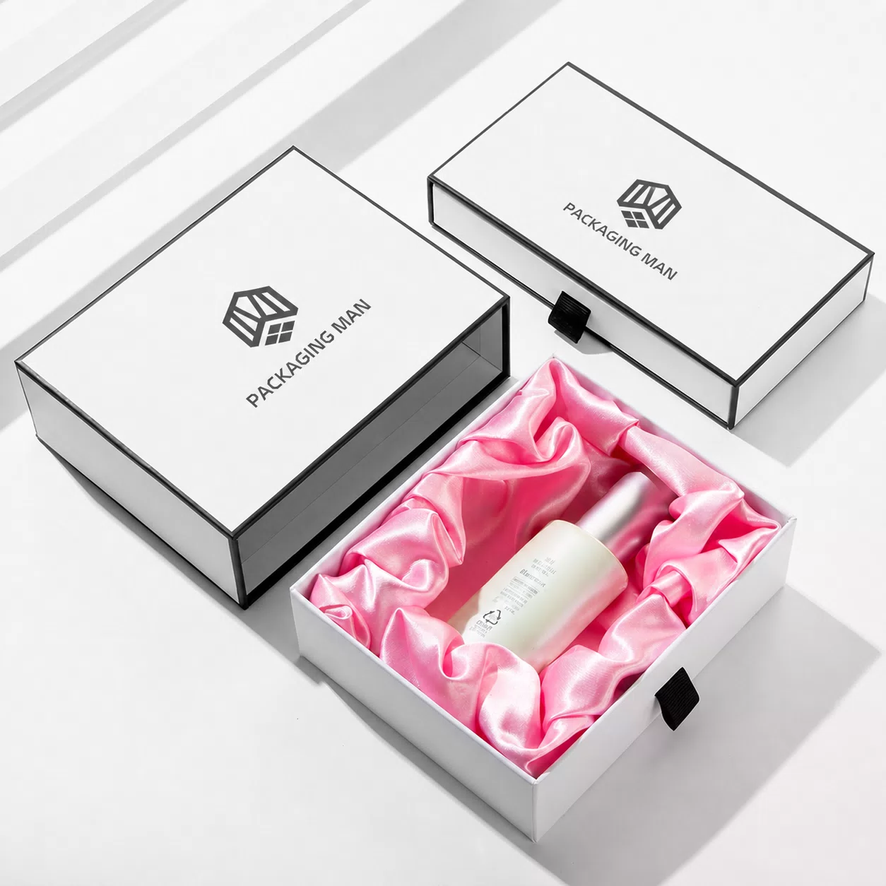 One box open revealing pink pleated satin lining and a white bottle, placed next to another closed box of the same design.