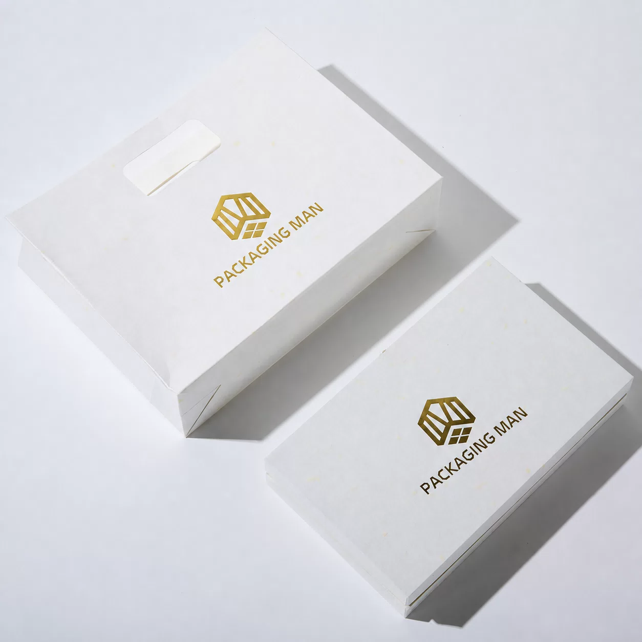 An overhead view showing the white paper bag and the closed white box arranged diagonally on a plain surface.
