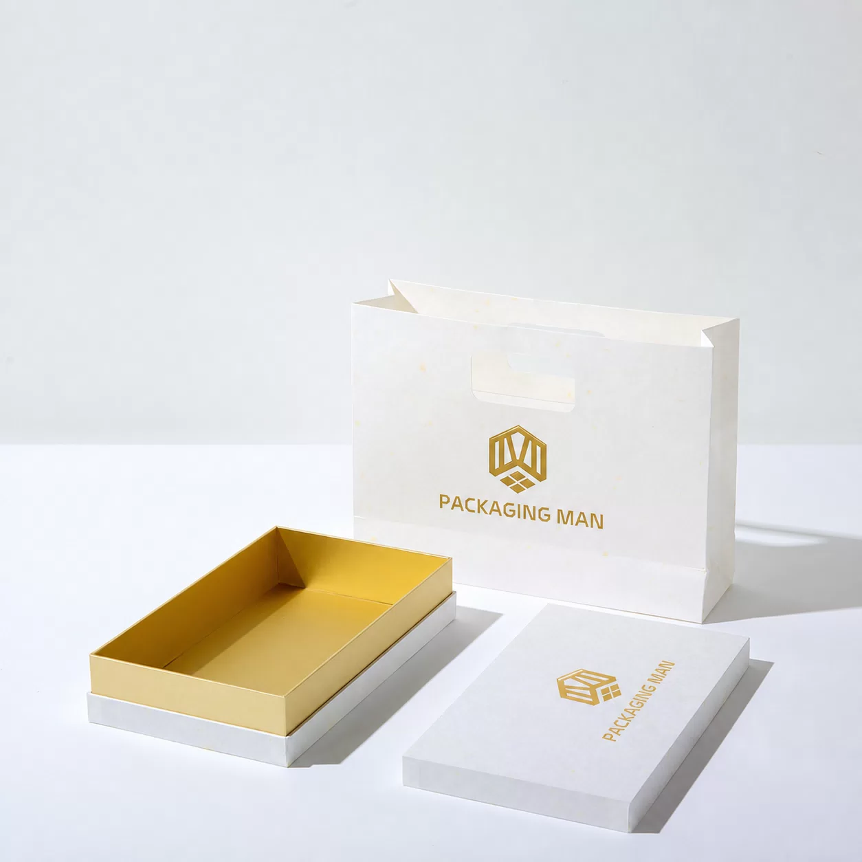 The components of the packaging are separated: the gold-lined bottom tray sits beside the detached white lid, with the bag standing behind them.